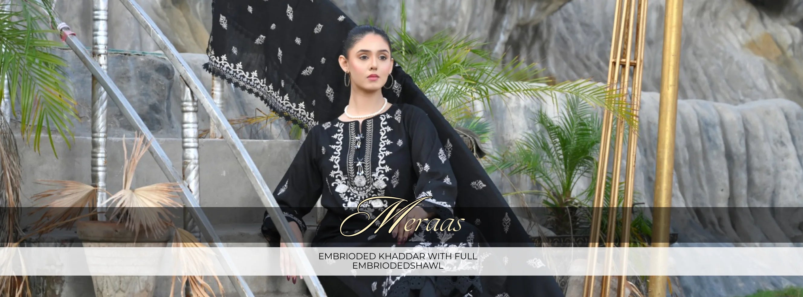 Woman in black embroidered outfit with 'Almeras' branding, standing outdoors with plants and a waterfall in the background.